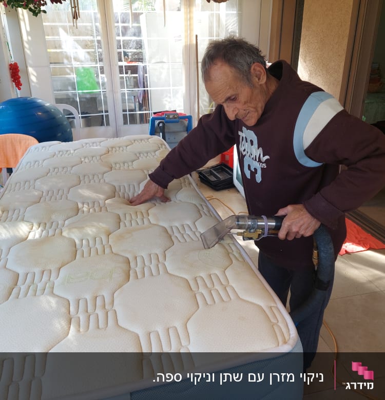 אדם מנקה מזרן עם שואב אבק ידני